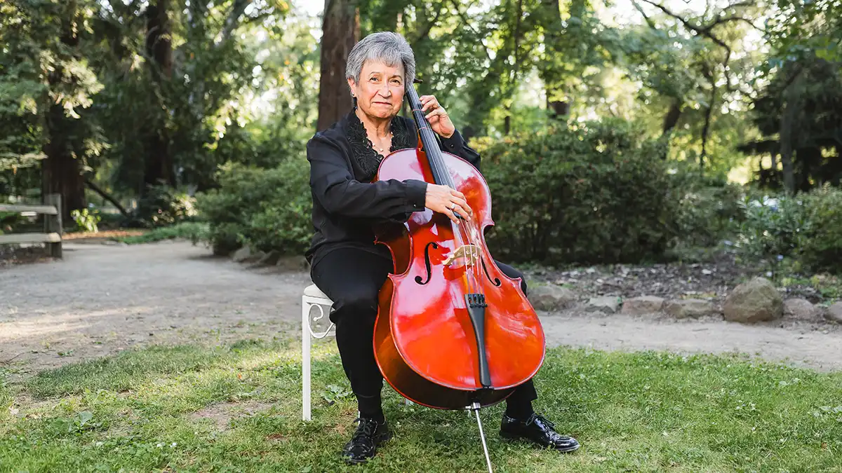 A Hispanic woman sits outdoors with a cello.