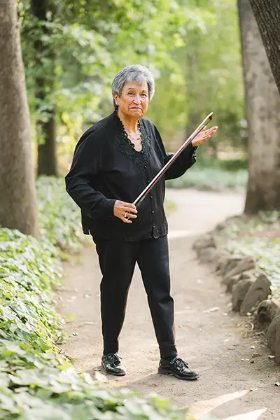 A woman stands on an outdoor walking path holding the bow for a stringed instrument.