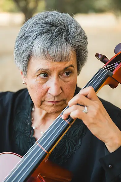 A Hispanic woman presses the strings of a cello.
