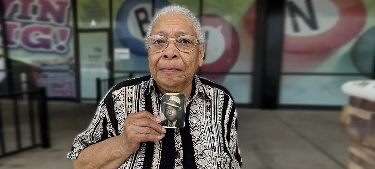 An older African American hwoman holds a black and white photo of her father