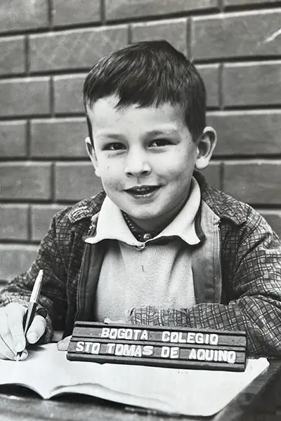 A boy holds a pen over a notebook in a vintage elementary school photo.