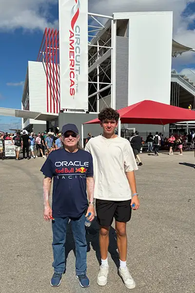 A teen boy stands with an older man at an outdoor event venue.