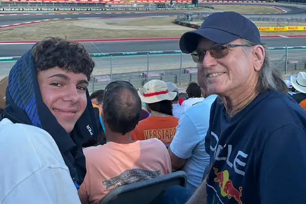 An older man sits with a teen boy in the stands of a racetrack.