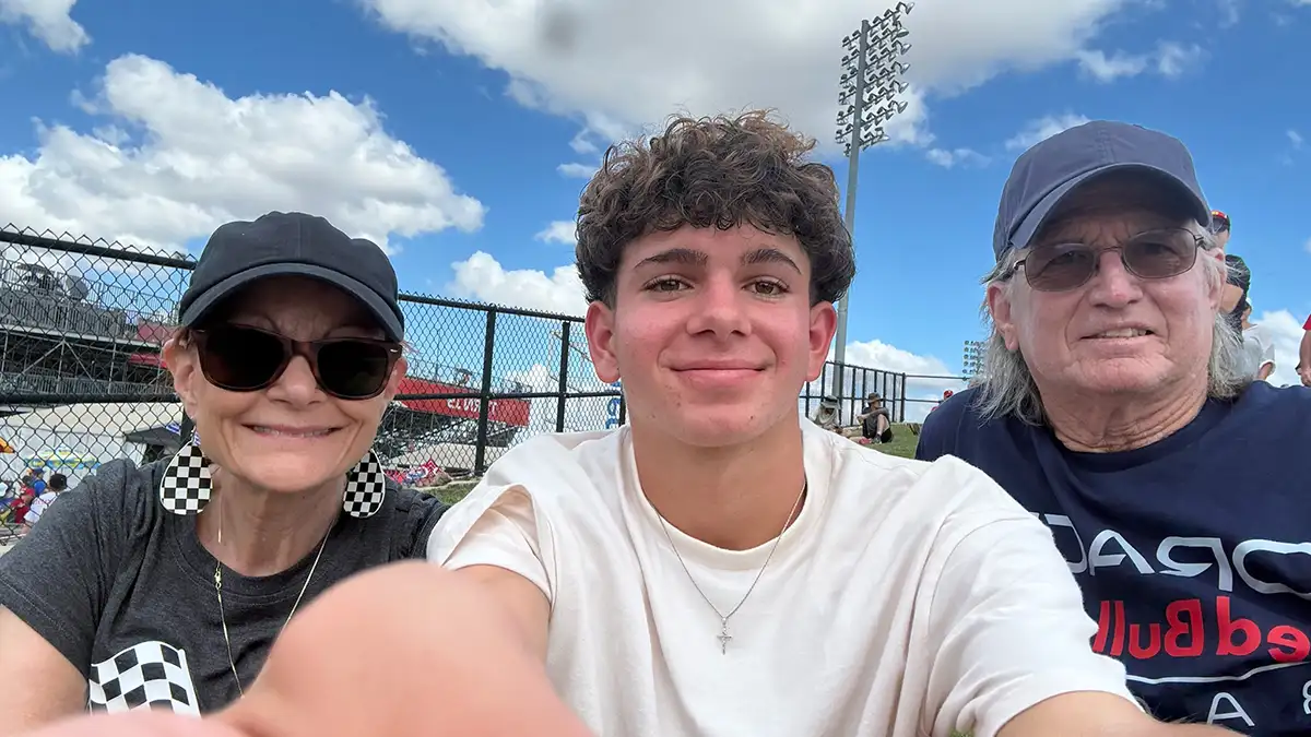 A teen boy takes a selfie with an older man and woman at a racetrack.