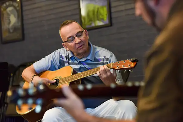 An older man plays guitar with an instructor.