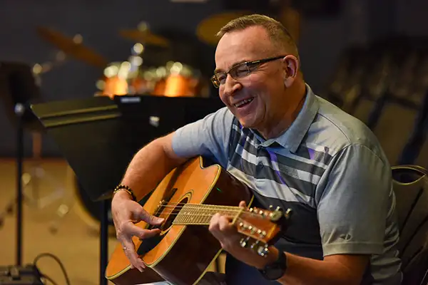 A man smiles while playing guitar.