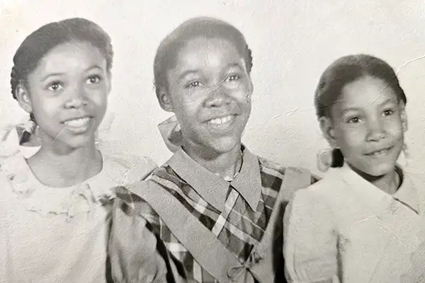 Three young Black girls in dresses smile in a black-and-white photo