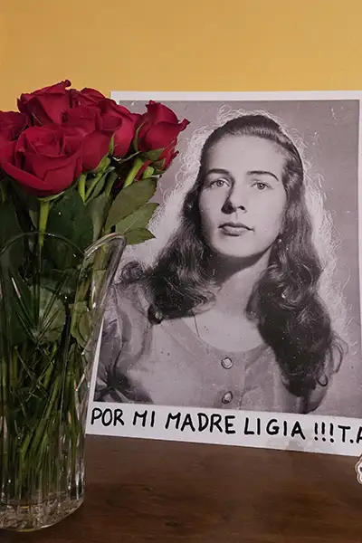 A vintage photo of a young woman sits on a table next to red roses.