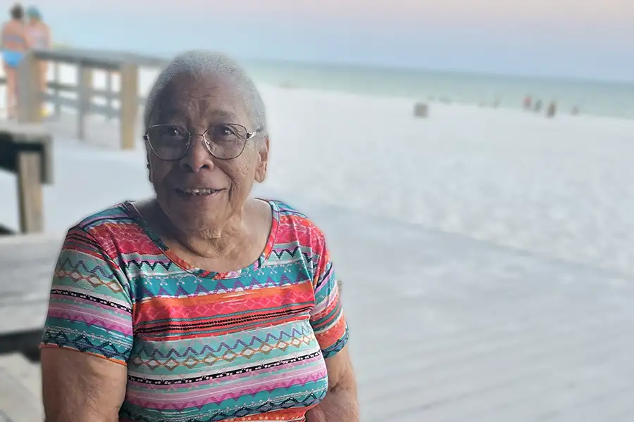 An older African American woman sits by the beach.