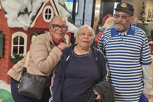 Three older adults stand in front of Christmas decorations