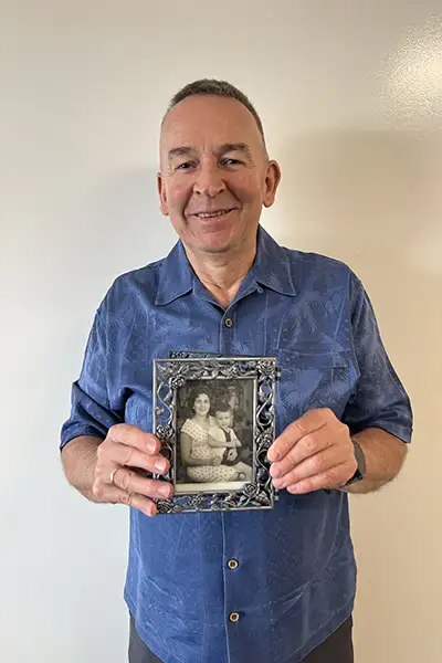 An older man holds a vintage photo of a mother and son.