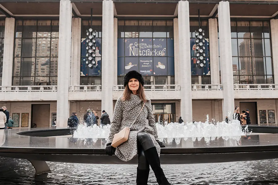 A woman sits outside near fountains and a Nutcracker ballet sign.