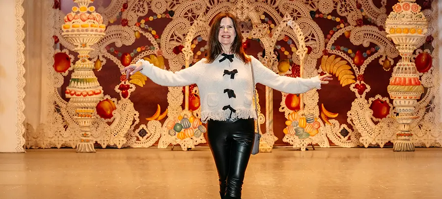 A woman stands with her arms extended in front of a set design for the Nutcracker ballet.