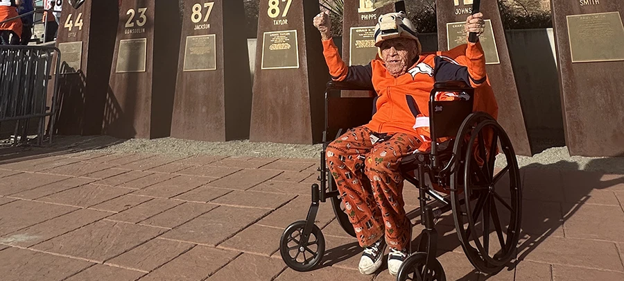 An older gentleman in a wheelchair wears Denver Broncos gear.