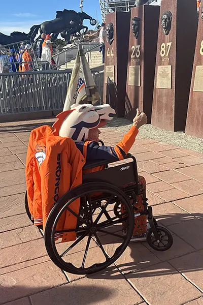 A man wearing Denver Broncos gear looks at bronze busts of football players from his wheelchair.