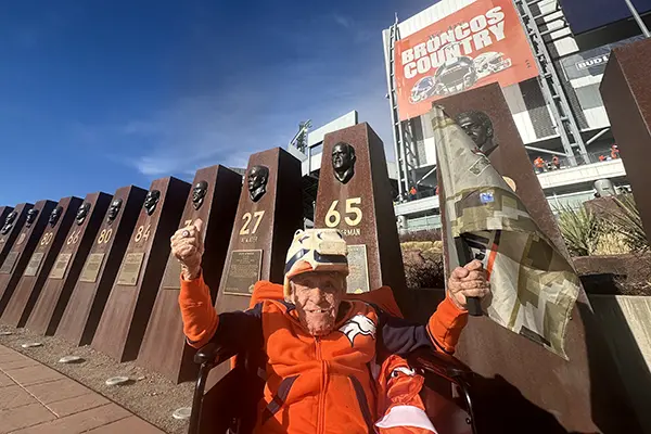A man wearing orange sits in front of the Denver Broncos football stadium.