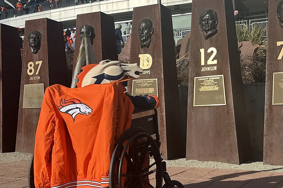 A person in a wheelchair wearing Denver Broncos gear looks at bronze busts honoring football players.