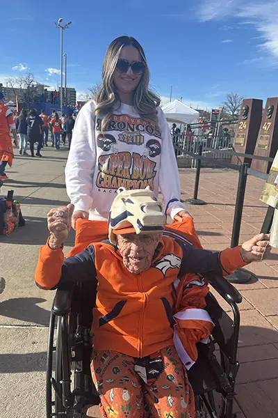A young woman pushes an older man in a wheelchair outside a football stadium.