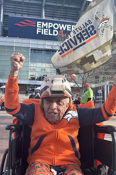 A man sits in a wheelchair waving a Denver Broncos flag.