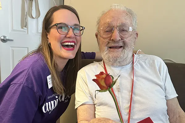 An older man holds a rose and a card while sitting next to a young woman