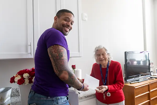 A young man delivers a card and rose to an older woman.