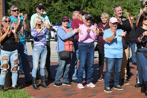 A group of people stand outdoors clapping.