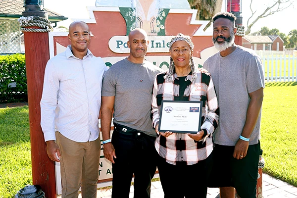 An older African American woman holds an award next to her three adult sons.