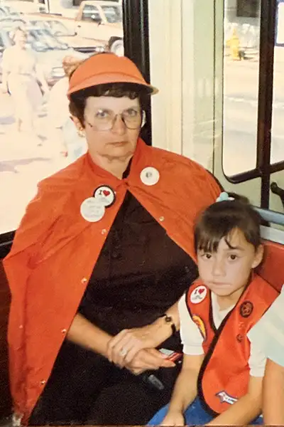 A woman wearing an orange poncho and visor sits on a bus with a girl.