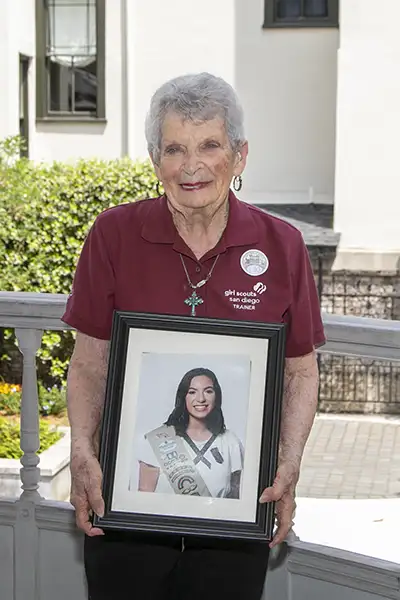 An older woman holds a framed photograph of a young Girl Scout.