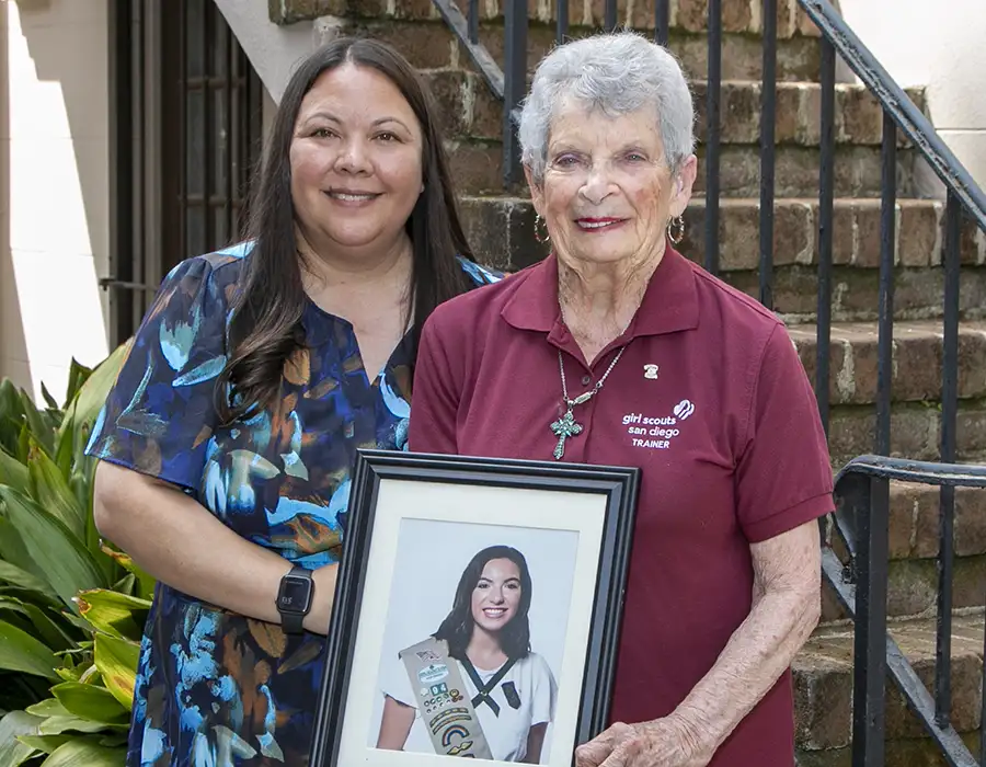 Two women stand holding a photo of a Girl Scout in uniform.
