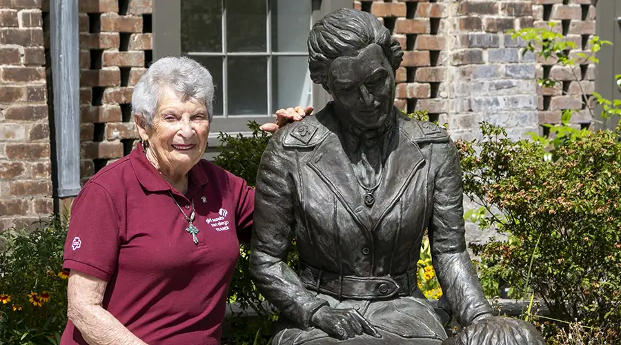 An older woman sits next to a statue of a woman.