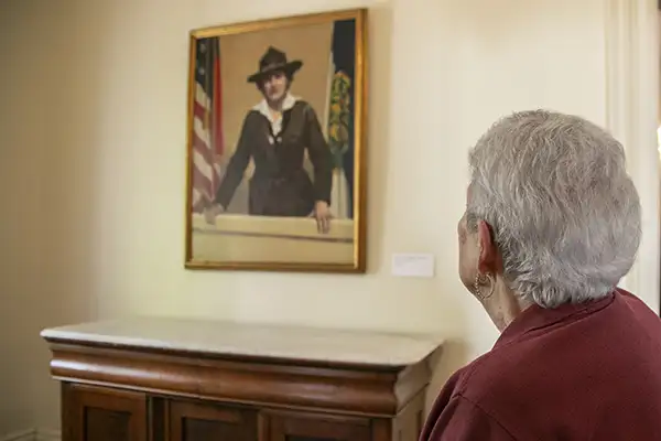 A woman looks at a portrait of a woman in a uniform.
