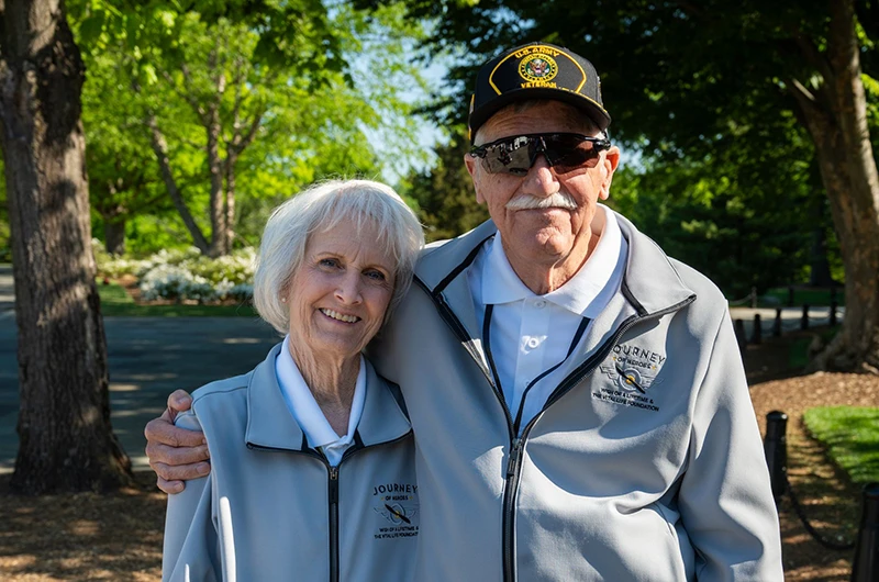 An older United States Army veteran stands arm in arm with his wife