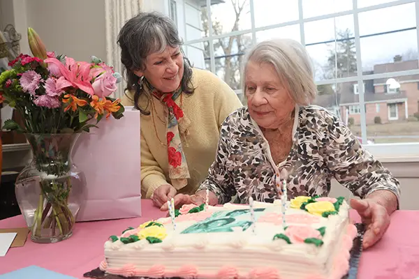 Two older women admire a birthday cake with candles.