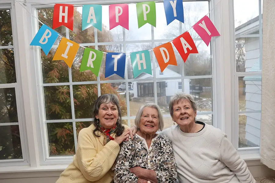 Three older women sit together under a birthday banner.
