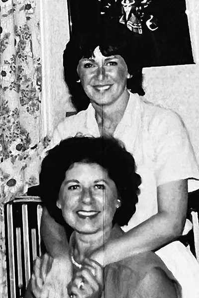 A woman stands behind another woman in a vintage photo.