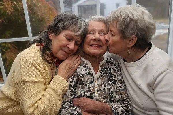 Three older women cuddle together.