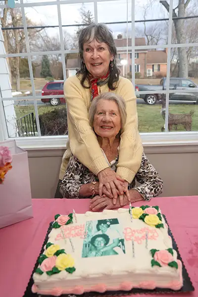 Two sisters stand behind a birthday cake with their photo on it.