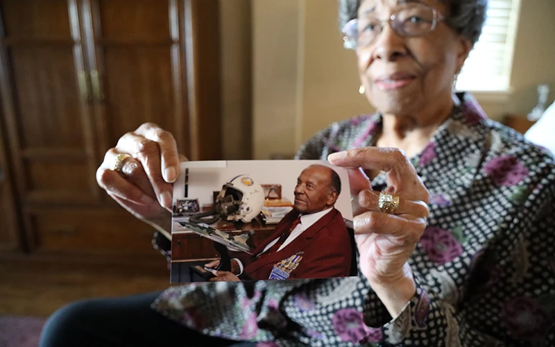 An older woman holds a photo of a man and a World War II pilot helmet