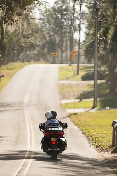 A motorcycle with two riders drives down a paved road, shown from behind
