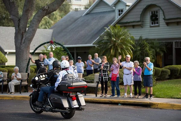 Two people on a motorcycle ride past a group of people who are waving