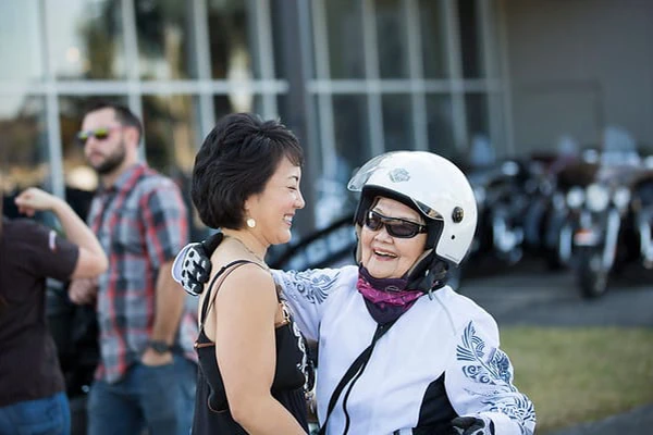 An older woman in motorcycle riding gear hugs a younger woman