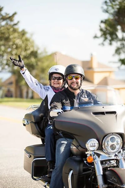 An older woman rides as a passenger on a motorcycle in full gear