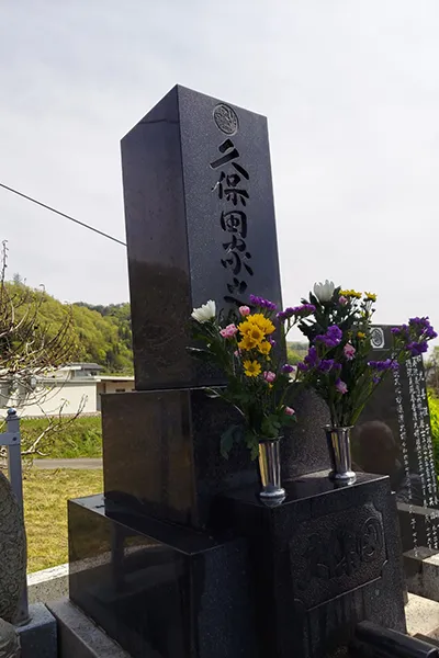 Bouquets of flowers sit on a grave with Japanese writing.