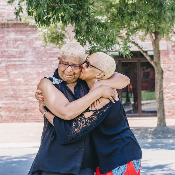 Two older African American women embrace as one kisses the other on the cheek