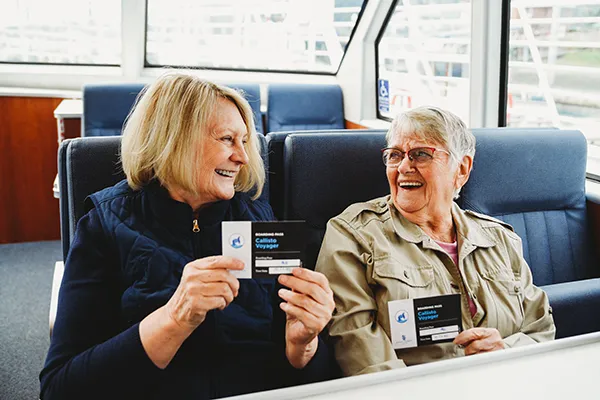 Two women smile at each other while seated in the passenger cabin of a tour boat.