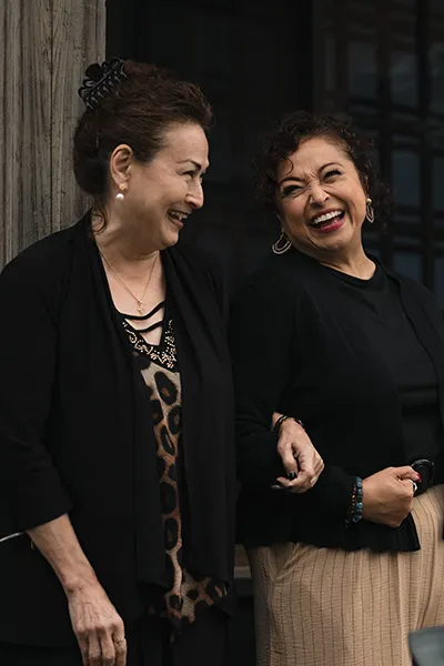 Two Asian women link arms and laugh together.