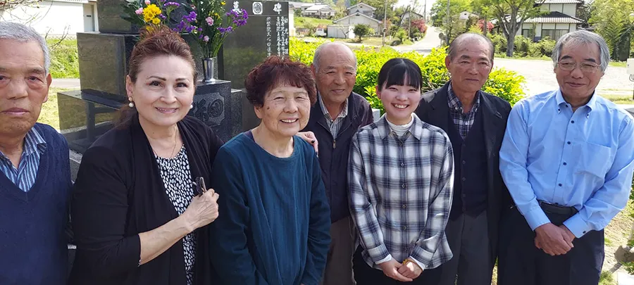 A group of Japanese people stand together at a gravesite in Japan.
