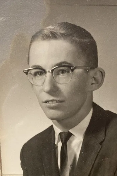 A vintage photograph of a teen boy wearing glasses and a suit.