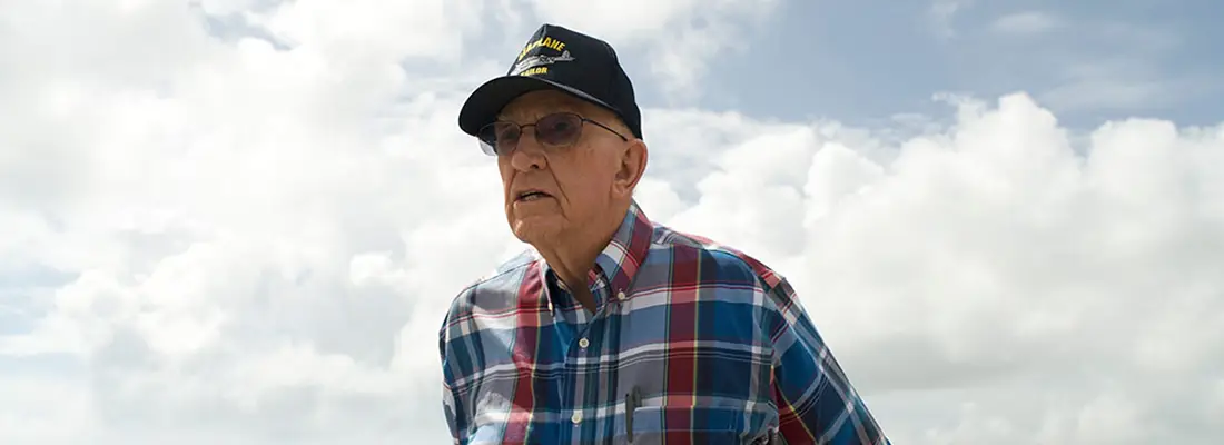 An older man wearing a WWII veteran baseball cap